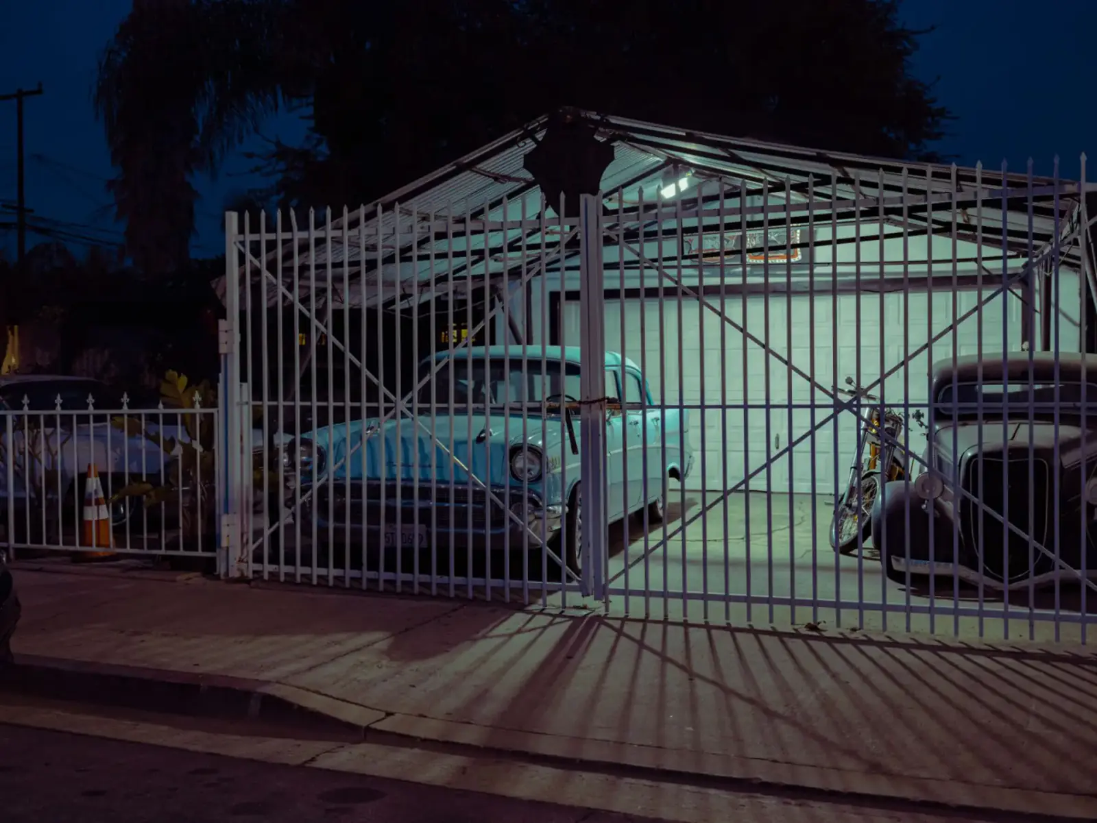 Light-coloured braced metal driveway gate closed across a residential drive at dusk