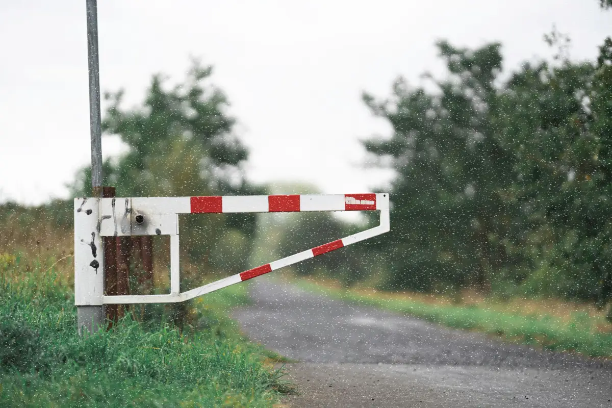 Red and white automated barrier gate arm lowered across a vehicle access lane