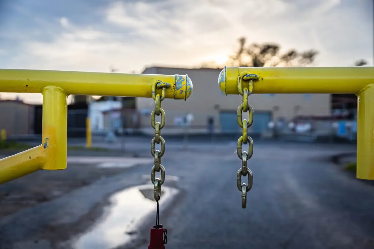 Yellow steel barrier gate with hanging chains closing a commercial lot entrance