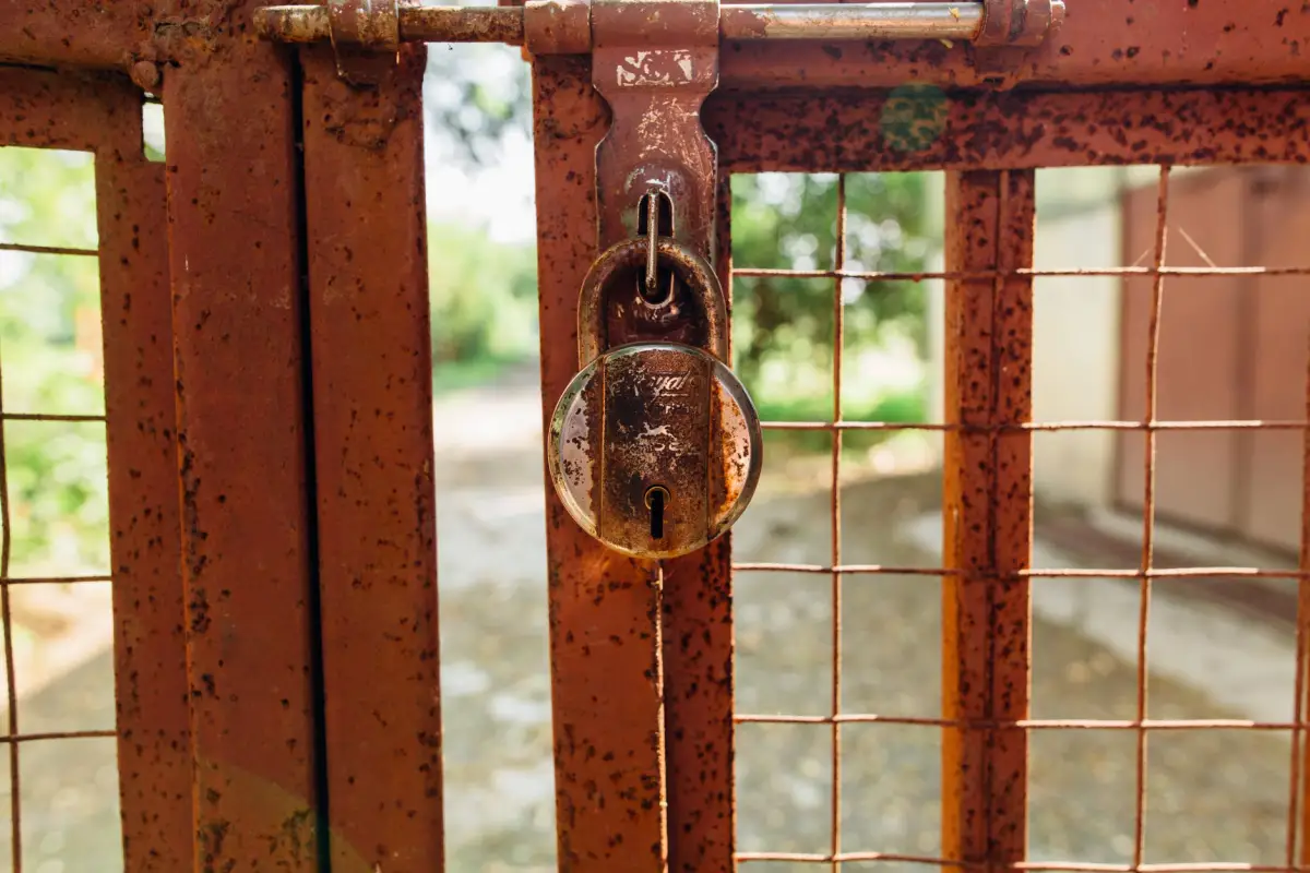 Rusted padlock and latch hardware on a corroded orange steel gate frame
