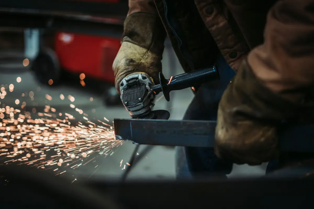 Gloved hands cutting a steel section with an angle grinder during a commercial gate repair