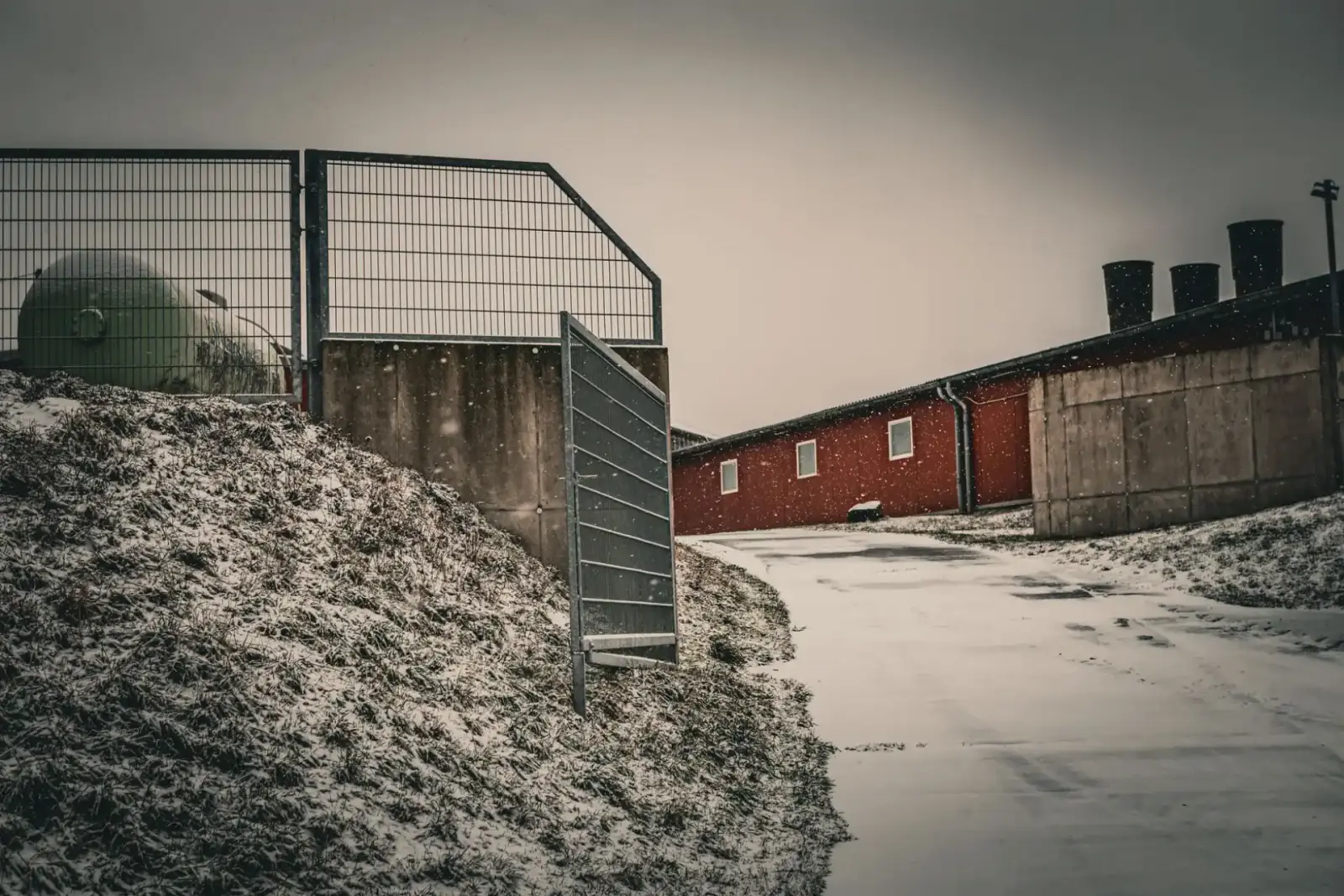 Metal security gate and perimeter fence at an industrial site with snow across the yard