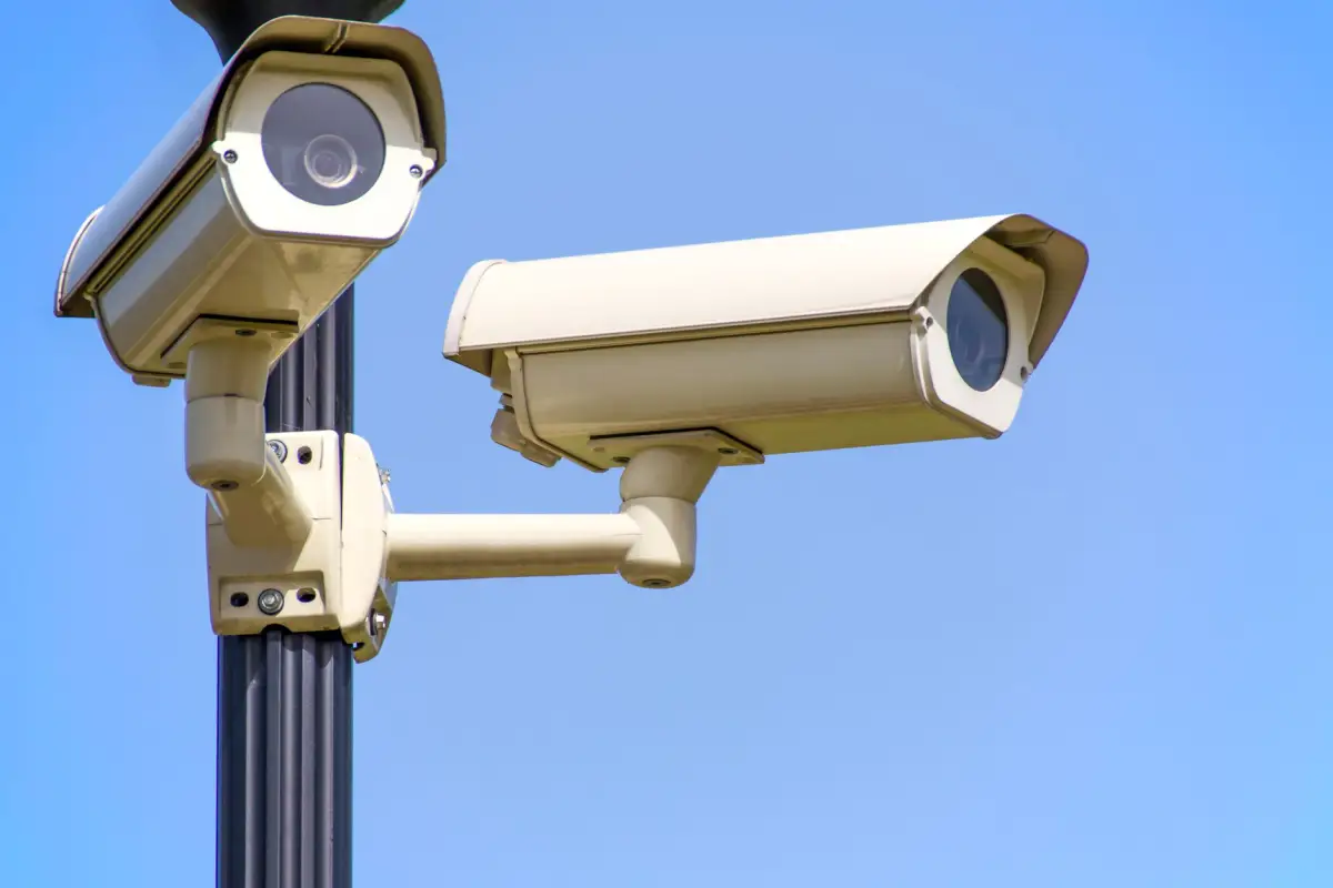 Two security cameras mounted on a pole covering a commercial gate approach