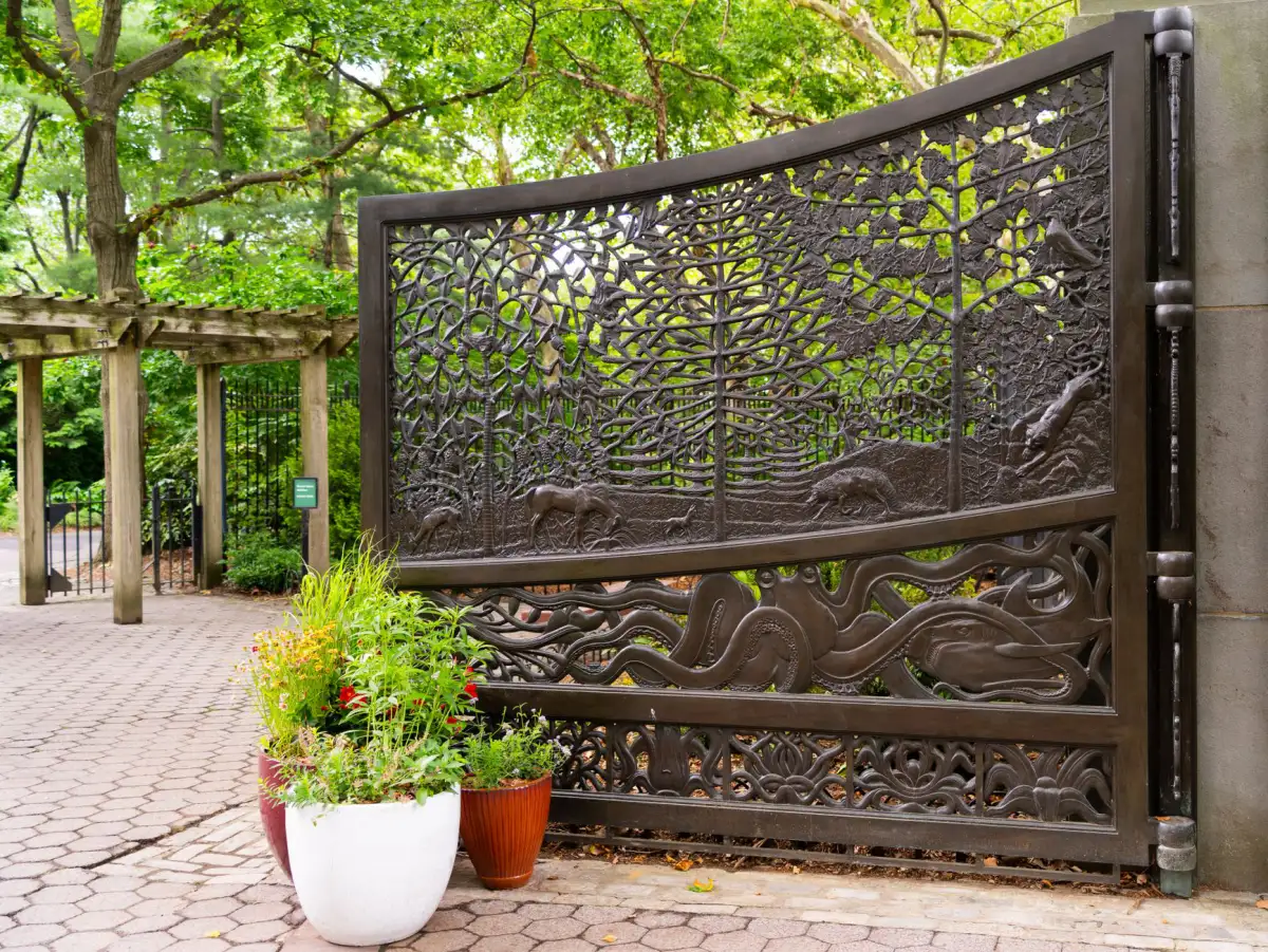 Custom bronze-finished metal gate with a cast tree-and-wildlife infill panel standing open on a paver drive