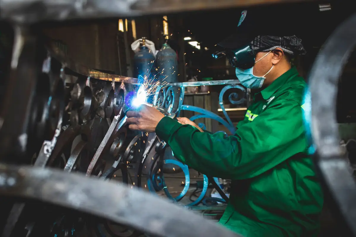 Fabricator in a welding hood and jacket welding an ornamental scroll panel for a custom metal gate