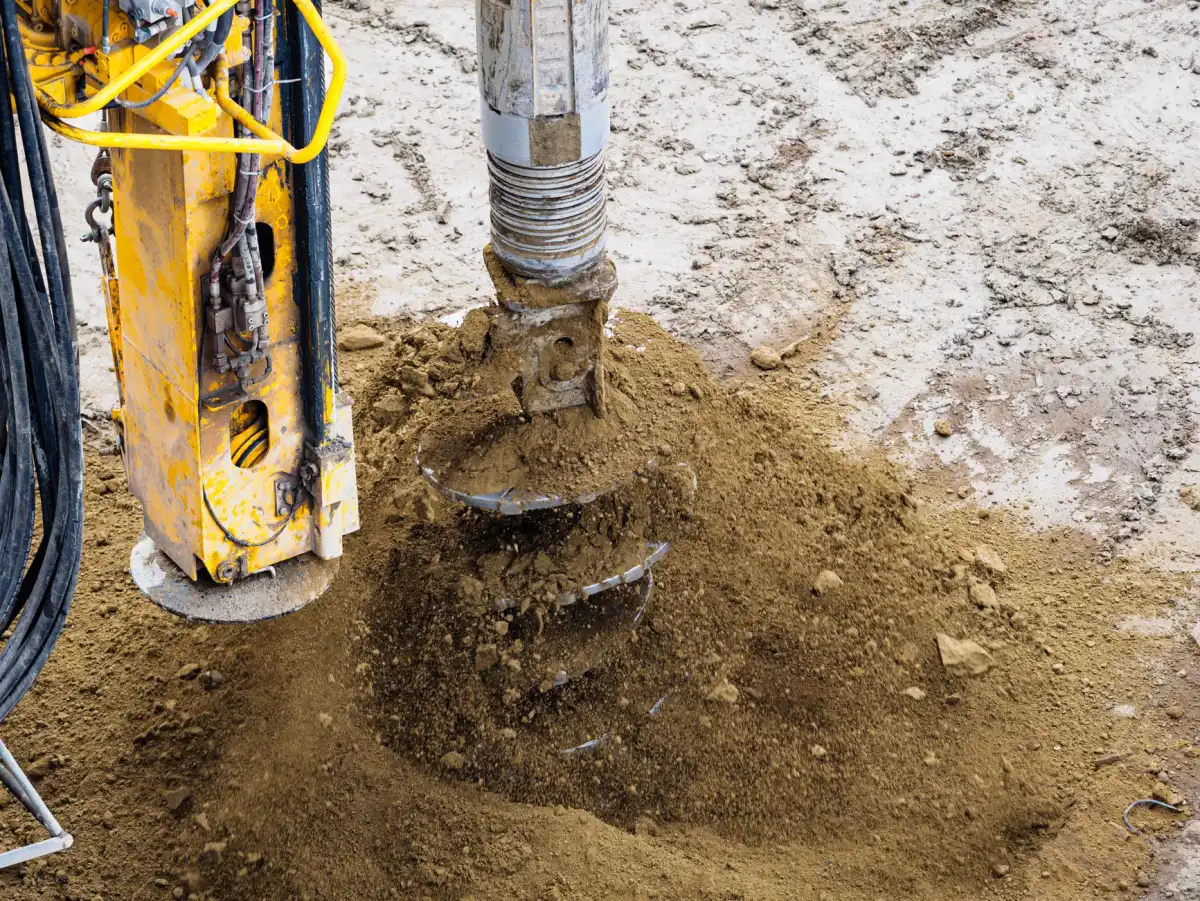 Hydraulic auger boring a gate post footing hole below the frost line beside a driveway