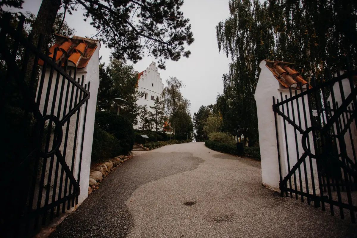 Black iron driveway gates standing open between rendered piers onto a gravel drive