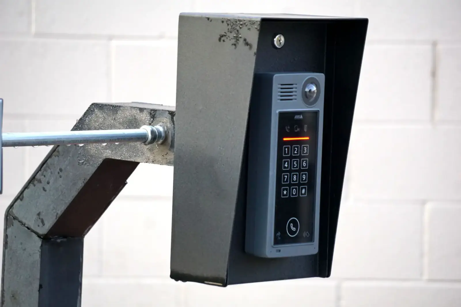 Video intercom and keypad entry unit mounted on a bracket beside a gate on a white block wall