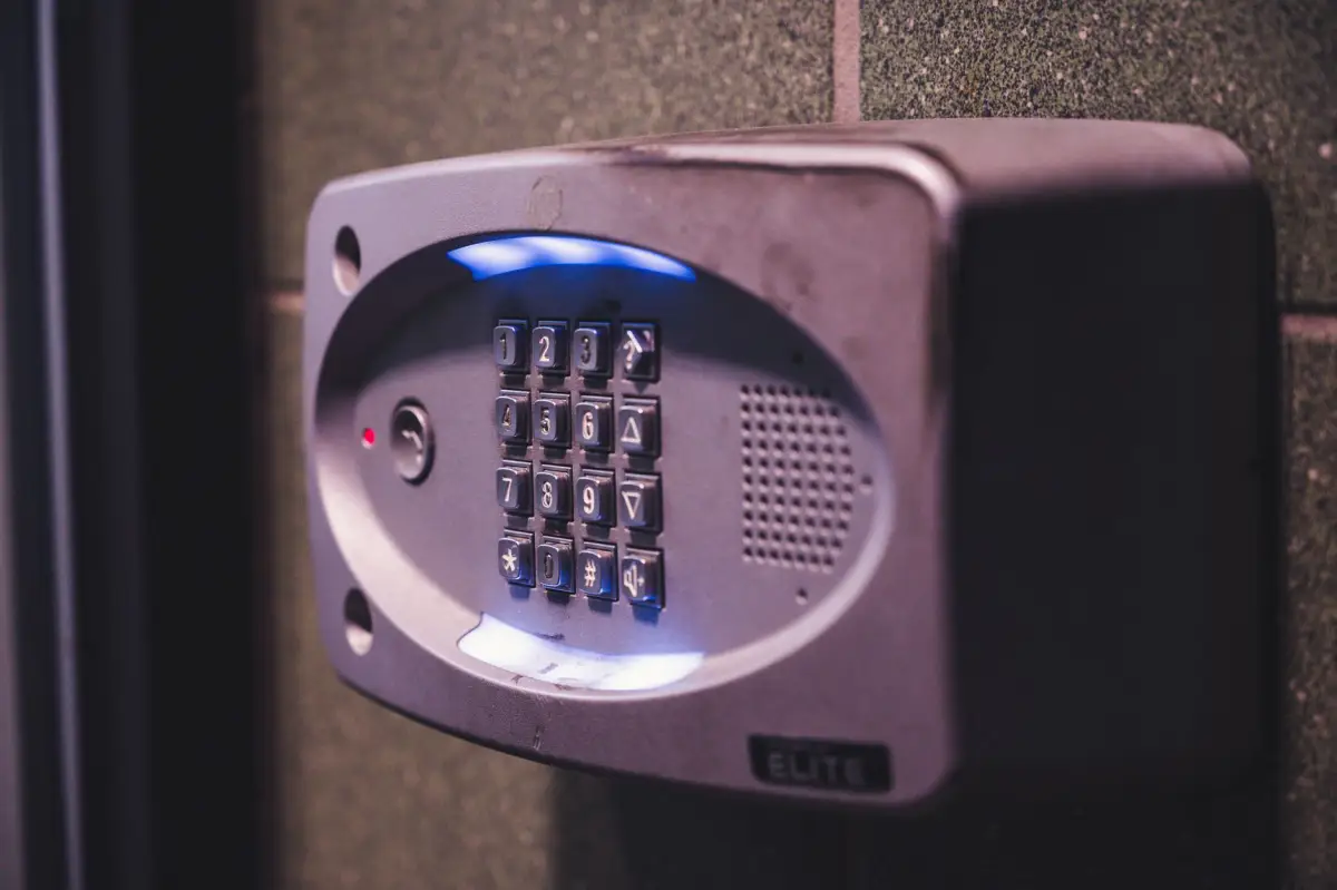 Backlit gate entry keypad with speaker mounted on a brick wall at a property entrance
