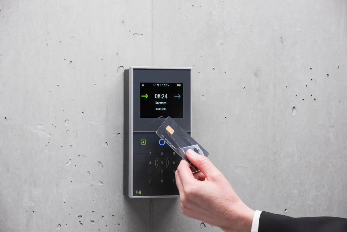 Hand presenting an access card to a wall-mounted reader with a lit display