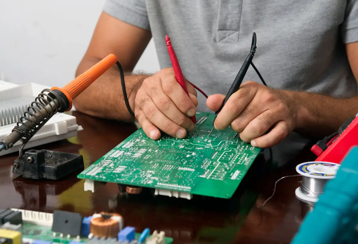 Technician soldering and probing a gate operator control board on a bench