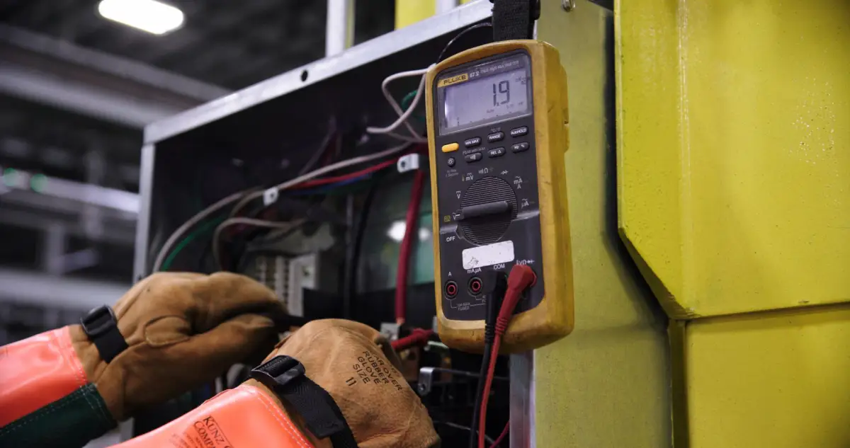 Gloved hands using a digital multimeter to test wiring inside an open gate operator control cabinet