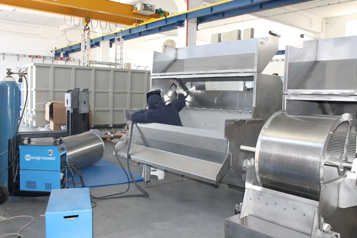 Welder fabricating large heavy-gauge steel assemblies under a gantry crane in an industrial shop