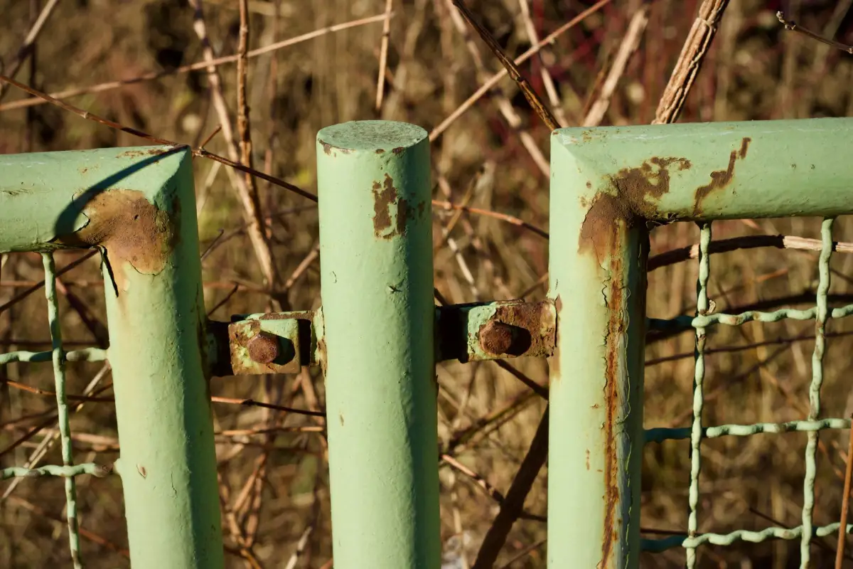 Corroded and flaking painted tube sections at a bolted joint on a metal gate frame