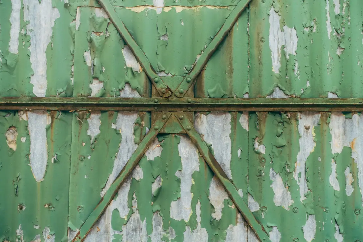Peeling paint and surface rust across the diagonal bracing of an old metal gate
