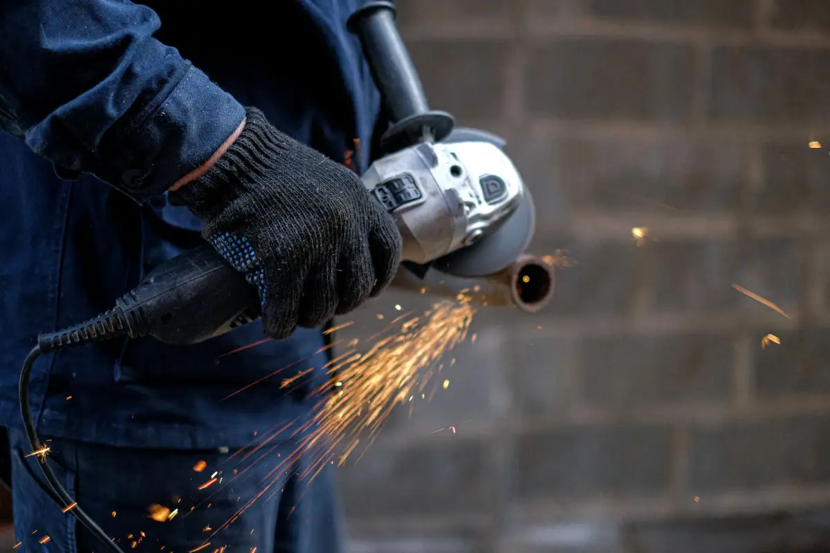 Gloved hands using an angle grinder on a steel gate section with sparks flying during a repair