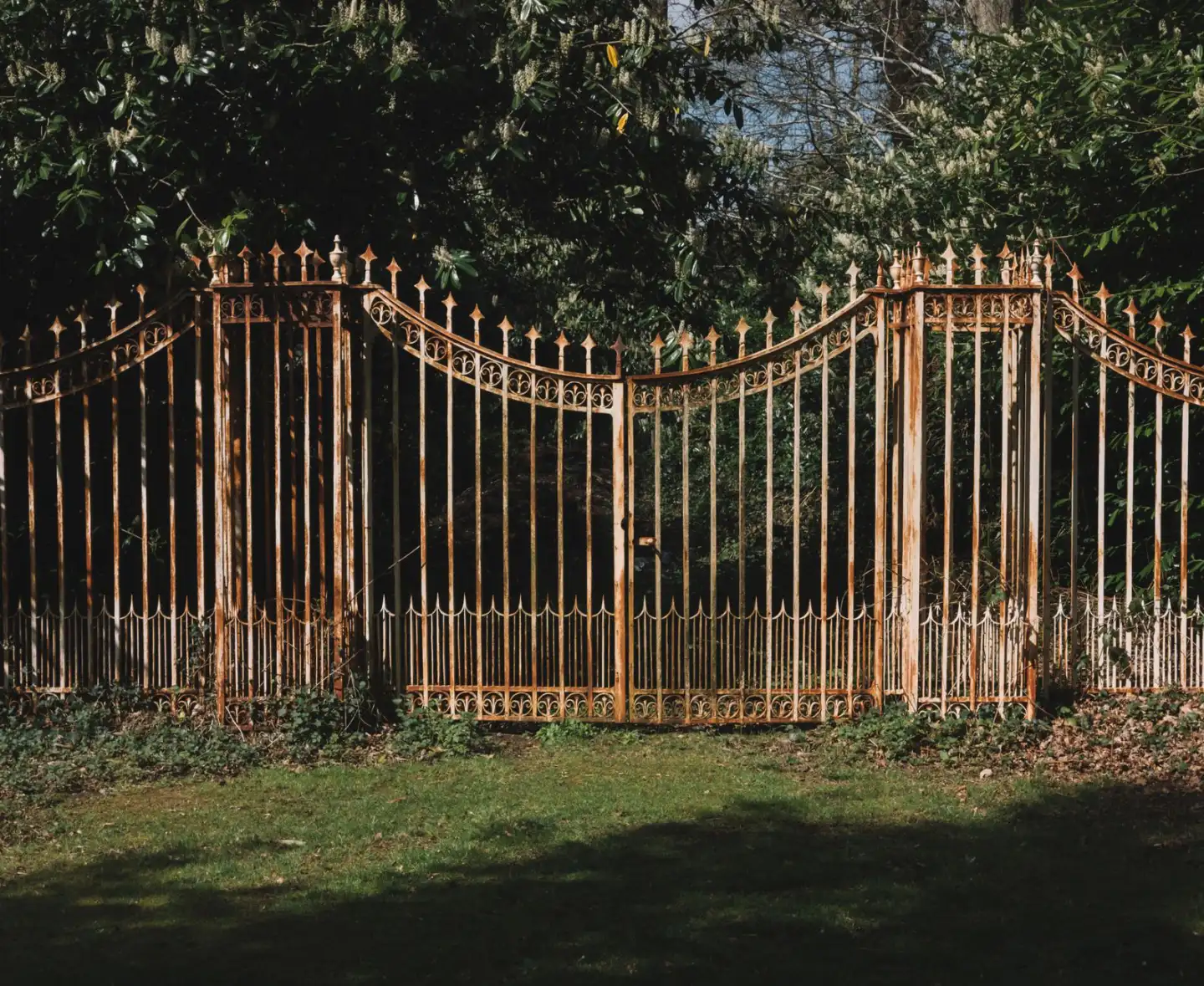 Rusted iron picket gate and fence leaning in a yard, showing corrosion and lost alignment