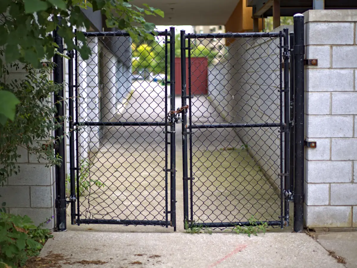 Black double pedestrian gate closing a narrow concrete walkway between two block walls