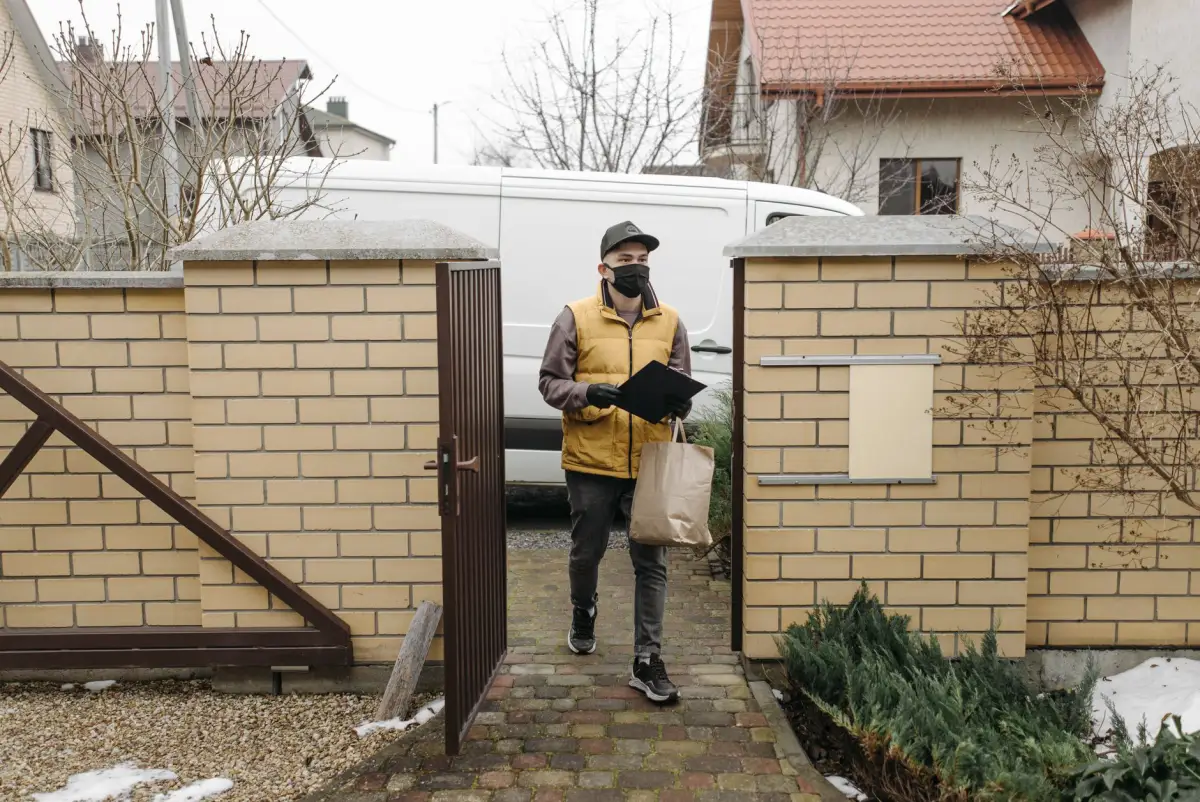Delivery driver stepping through an open pedestrian gate in a brick wall on a winter morning