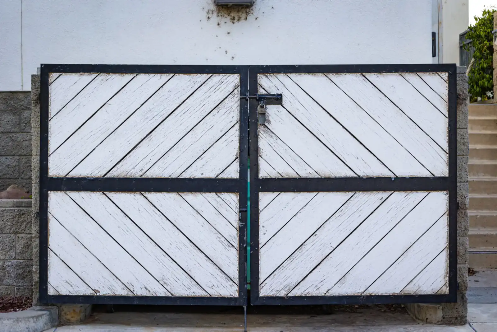White-panelled metal double security gate set between block walls at a property entrance
