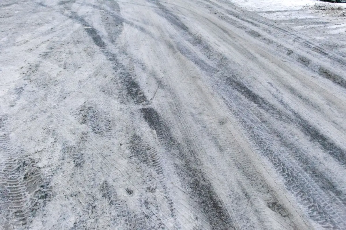Packed snow and ice with frozen tire tracks across a driveway apron where a slide gate track would sit