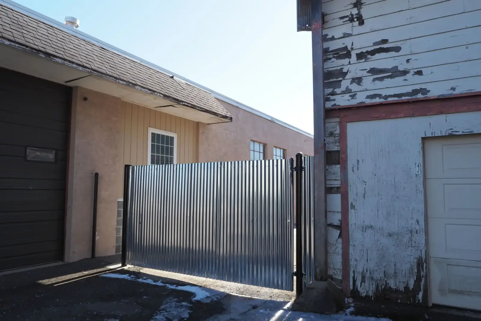 Corrugated metal sliding gate closed across a narrow side drive between a house and a garage