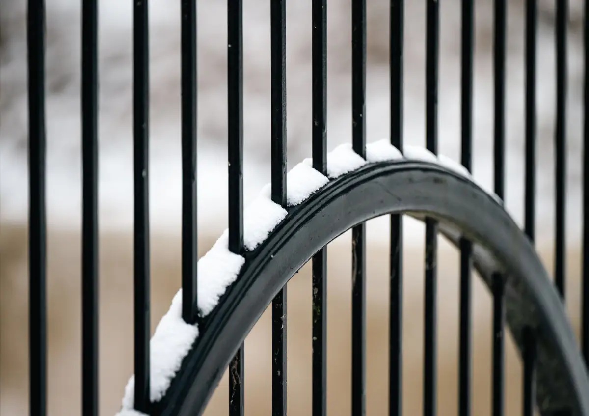 Snow packed along the curved top rail and pickets of a black metal gate after a storm