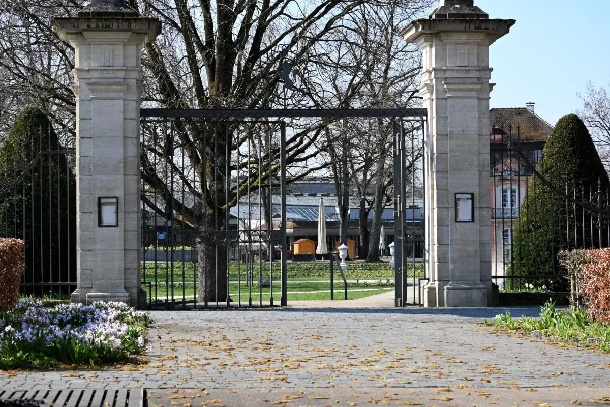 Tall double iron swing gates standing open between stone piers at a park entrance