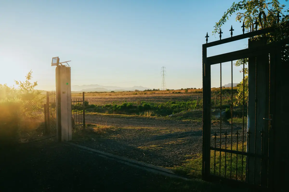 Single black metal swing gate standing open at a property entrance at sunrise
