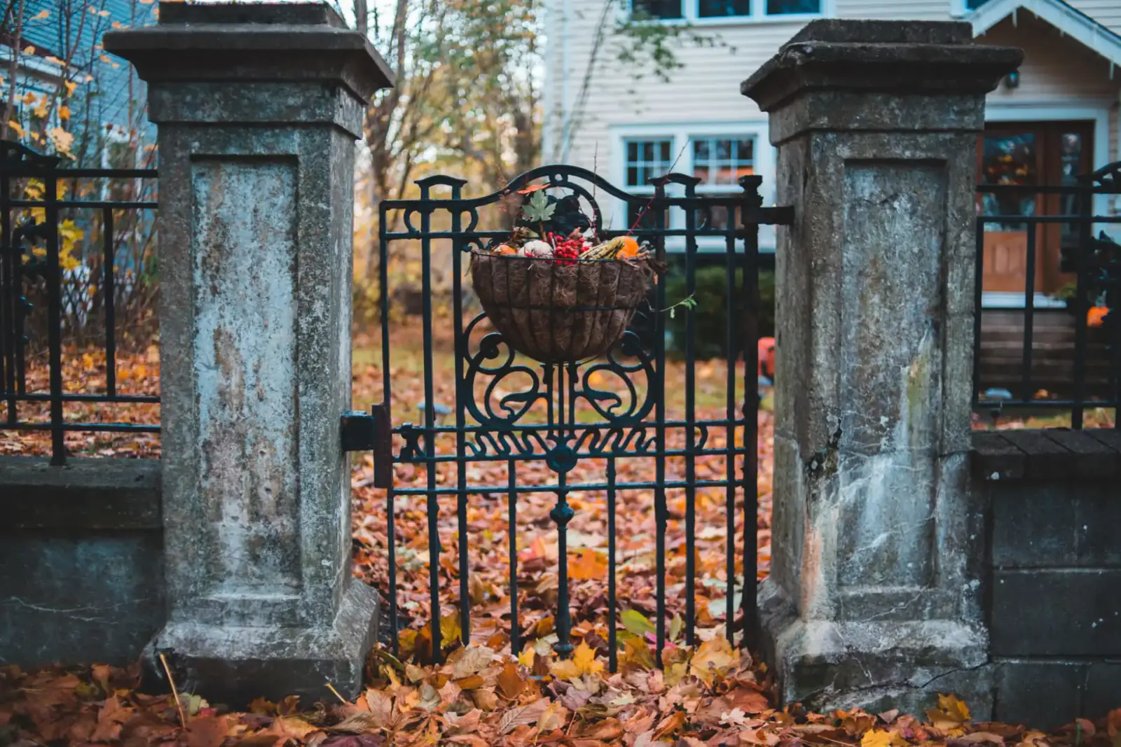 Ornamental iron swing gate hung between stone piers with autumn leaves on the ground in front of a house