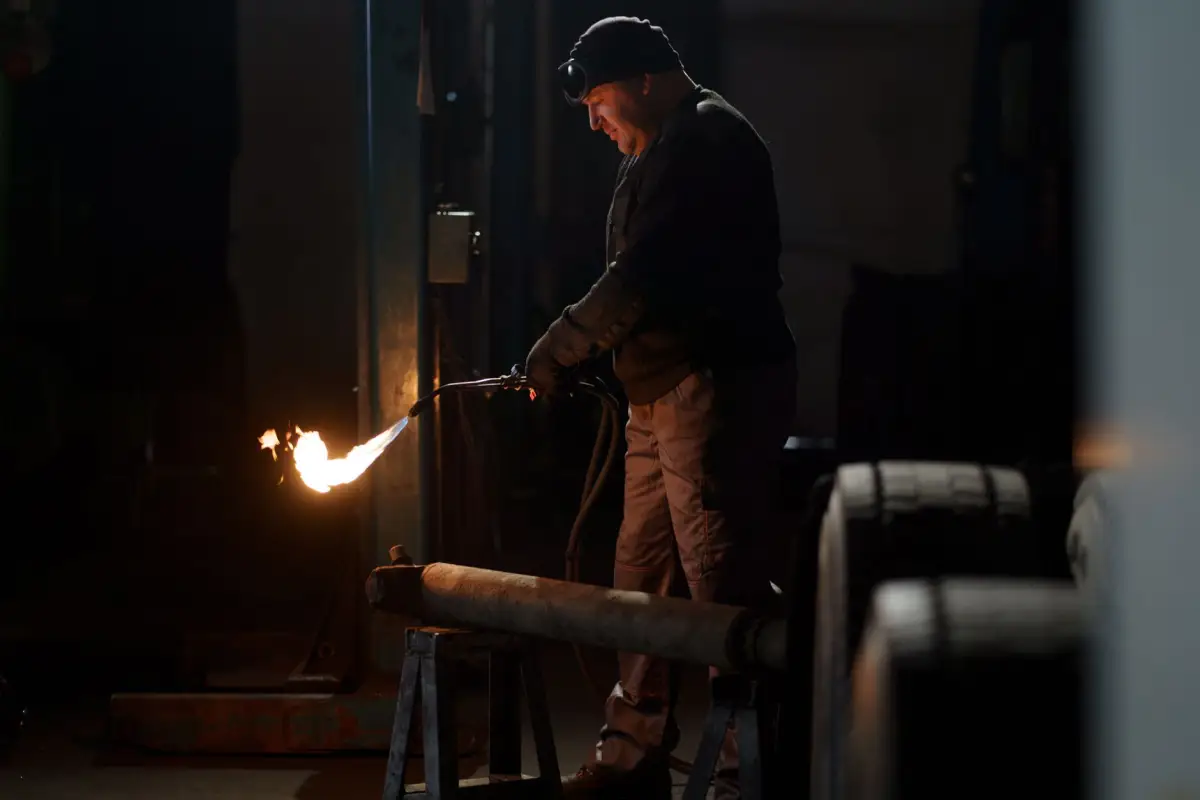 Blacksmith heating a steel bar with a torch at the forge while making ornamental gate components
