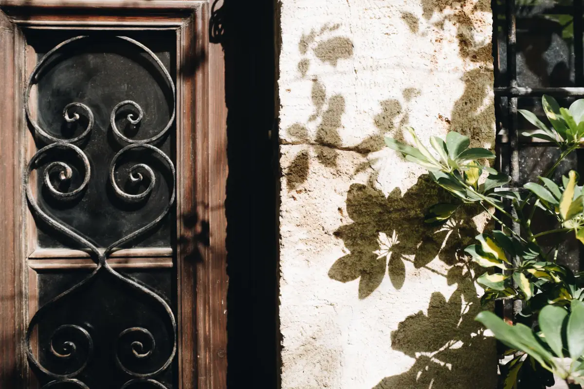 Black ornamental iron scroll panel set into a weathered wall beside foliage